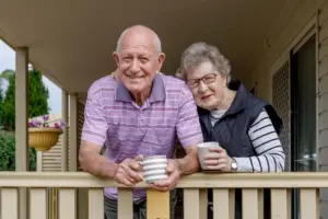 Elderly couple smiling and holding coffee cups, symbolizing the importance of managing osteoporosis for a happy, active life